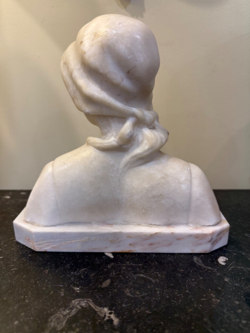 An off-white carved alabaster bust depicting a young woman wearing a bonnet, resting on an integral octagonal stone base. View III