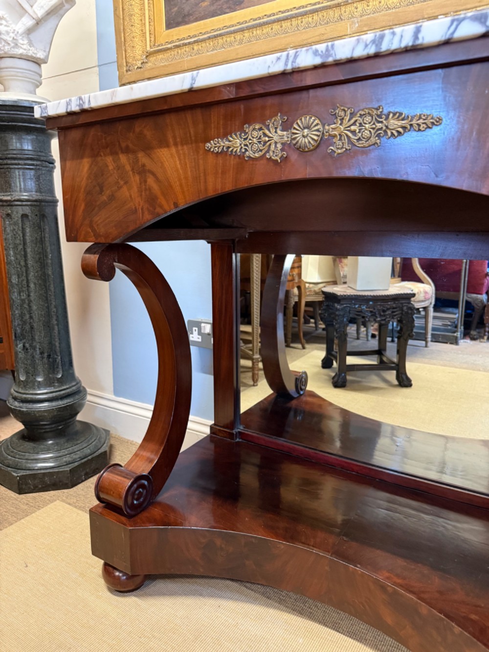 A 19th-century mahogany console table featuring a white veined marble top, an ornate brass mount on the apron, curved scroll front supports, a plinth base, and a mirrored back. View III