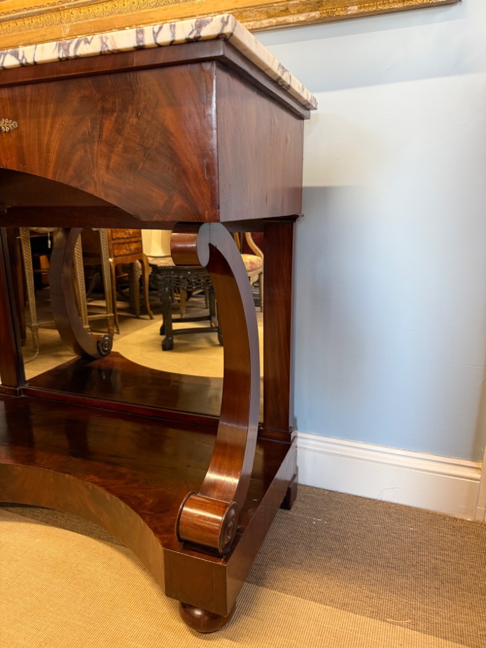 A 19th-century mahogany console table featuring a white veined marble top, an ornate brass mount on the apron, curved scroll front supports, a plinth base, and a mirrored back. View IV