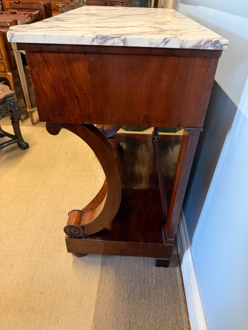 A 19th-century mahogany console table featuring a white veined marble top, an ornate brass mount on the apron, curved scroll front supports, a plinth base, and a mirrored back. View V