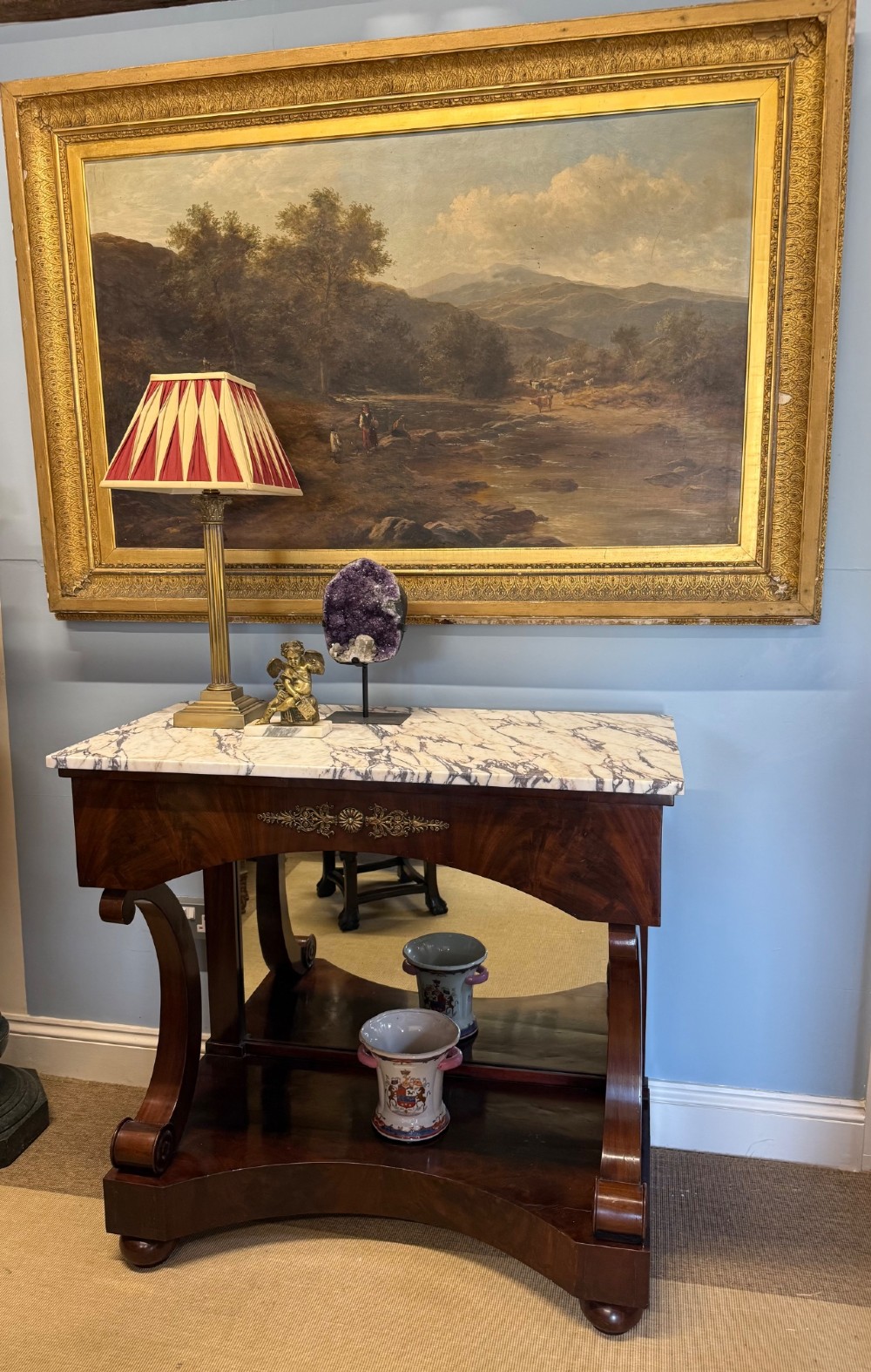 A 19th-century mahogany console table featuring a white veined marble top, an ornate brass mount on the apron, curved scroll front supports, a plinth base, and a mirrored back. View VII