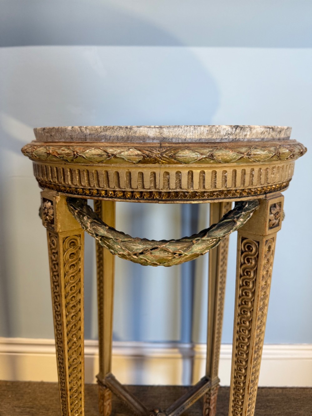 A tall 19th-century French Neoclassical style plant stand featuring a circular grey marble top, carved cream and parcel-gilded legs with swags, and a central X-stretcher. View VII