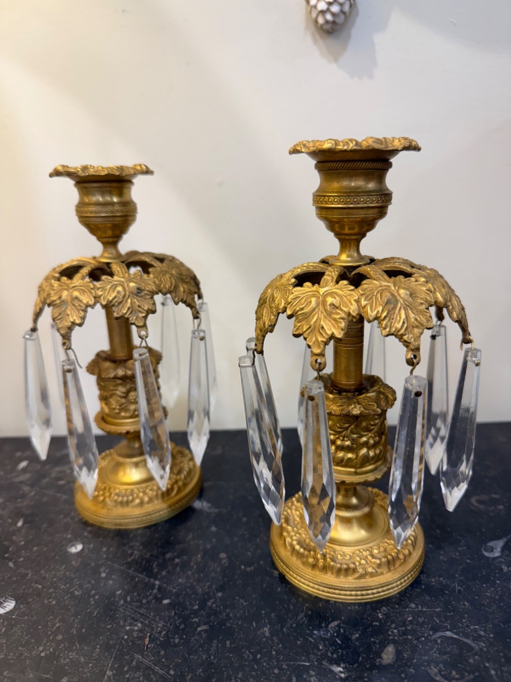 A pair of 19th-century gilt bronze ormolu candlesticks featuring acanthus leaf crowns and suspended clear crystal prism lustres.