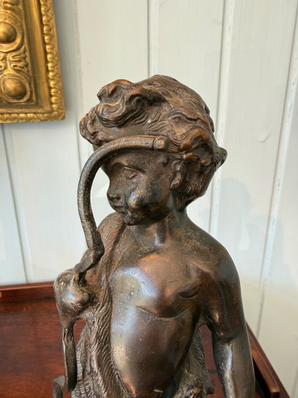 An antique dark bronze figural sculpture depicting a young cherub holding a bow and hunted game, standing on a square green marble base. View III
