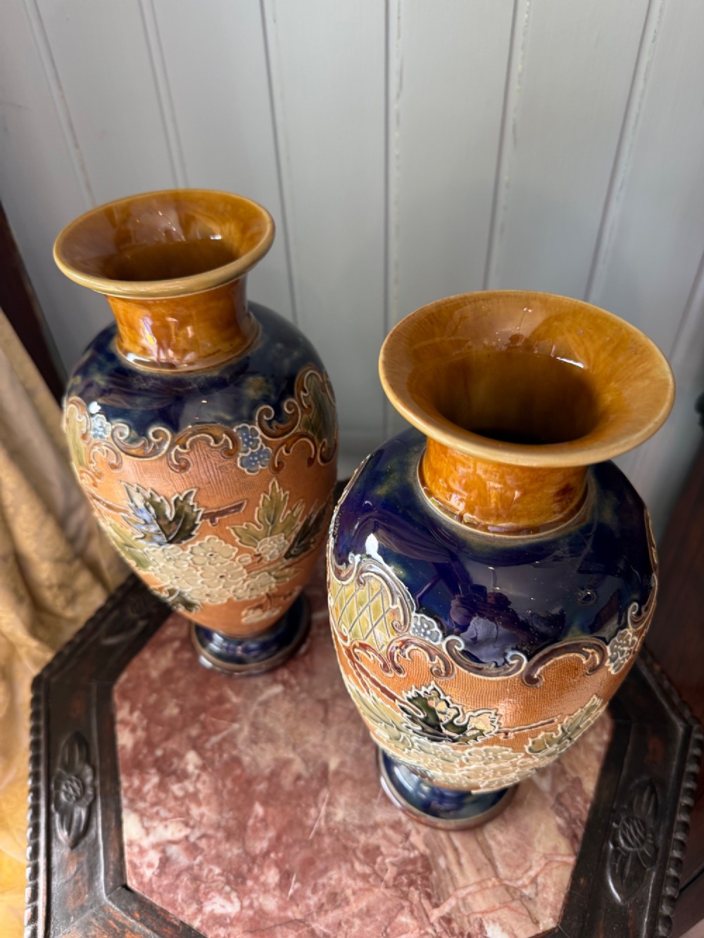 A pair of antique Royal Doulton stoneware vases featuring ochre bodies with raised floral relief decoration, flared rims, and cobalt blue accents. View II