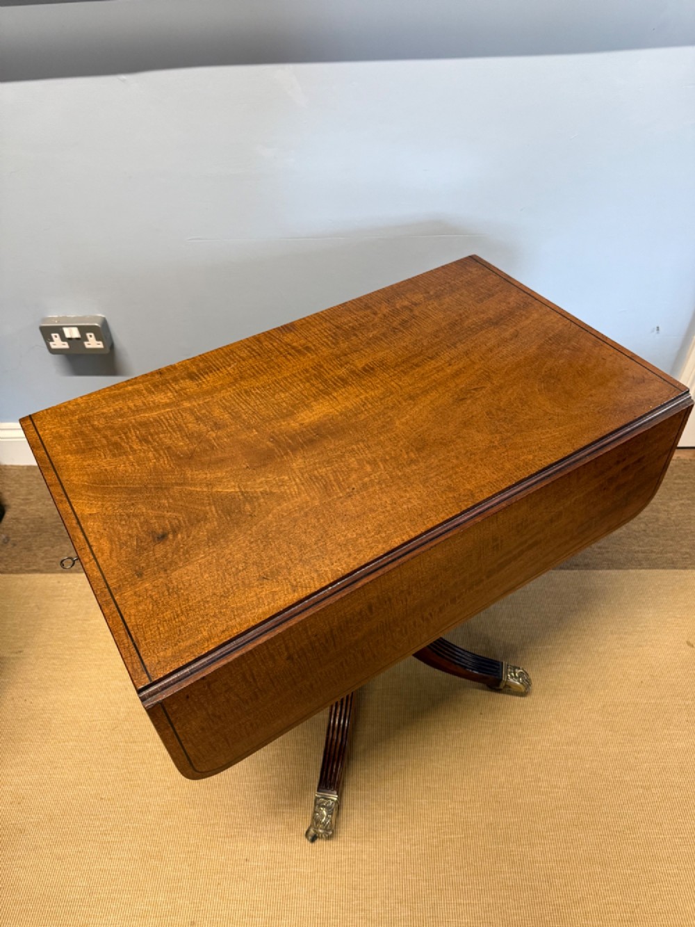 A Regency mahogany drop-leaf table featuring a turned central column, reeded quadform legs, and brass lion paw castors. View II