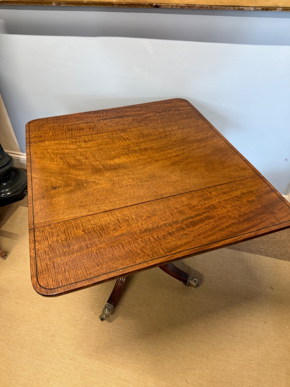 A Regency mahogany drop-leaf table featuring a turned central column, reeded quadform legs, and brass lion paw castors. View III