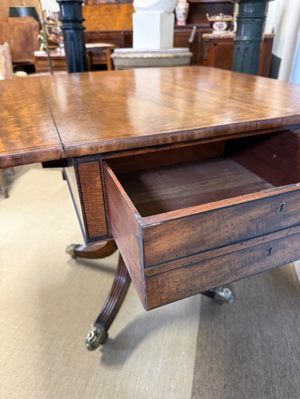 A Regency mahogany drop-leaf table featuring a turned central column, reeded quadform legs, and brass lion paw castors. View IV