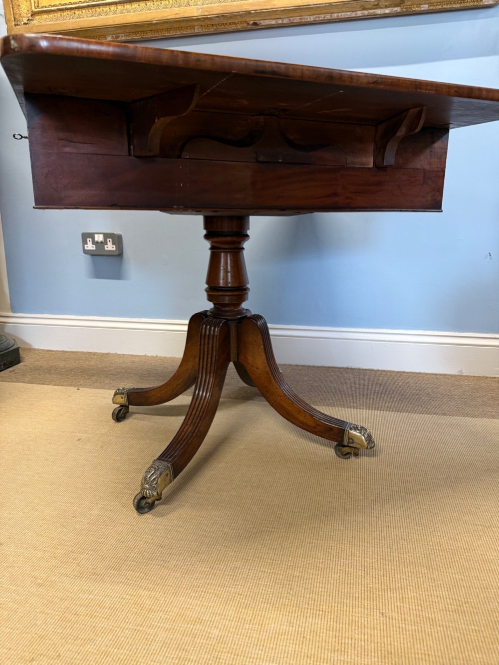 A Regency mahogany drop-leaf table featuring a turned central column, reeded quadform legs, and brass lion paw castors. View VI