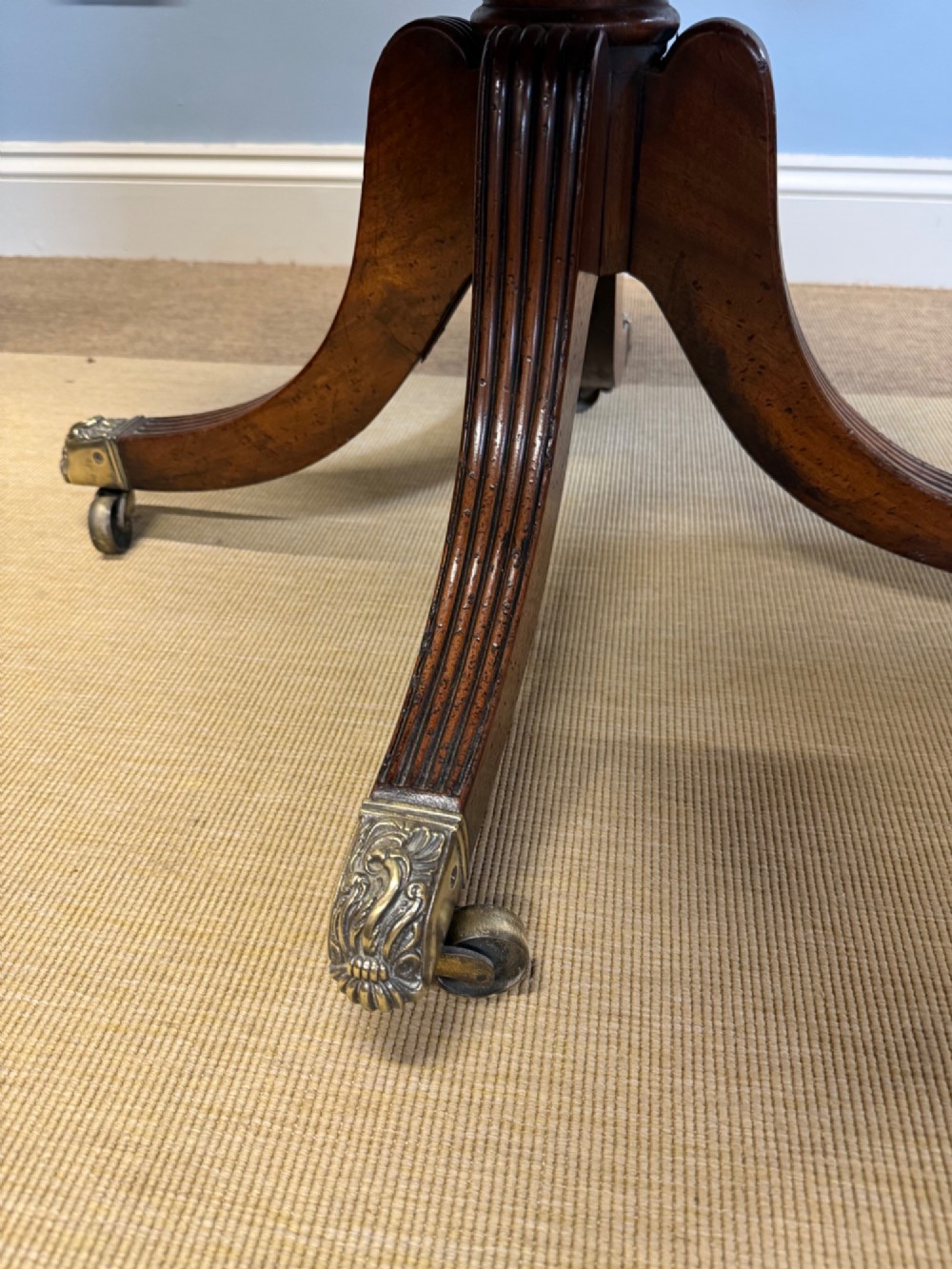A Regency mahogany drop-leaf table featuring a turned central column, reeded quadform legs, and brass lion paw castors. View VII