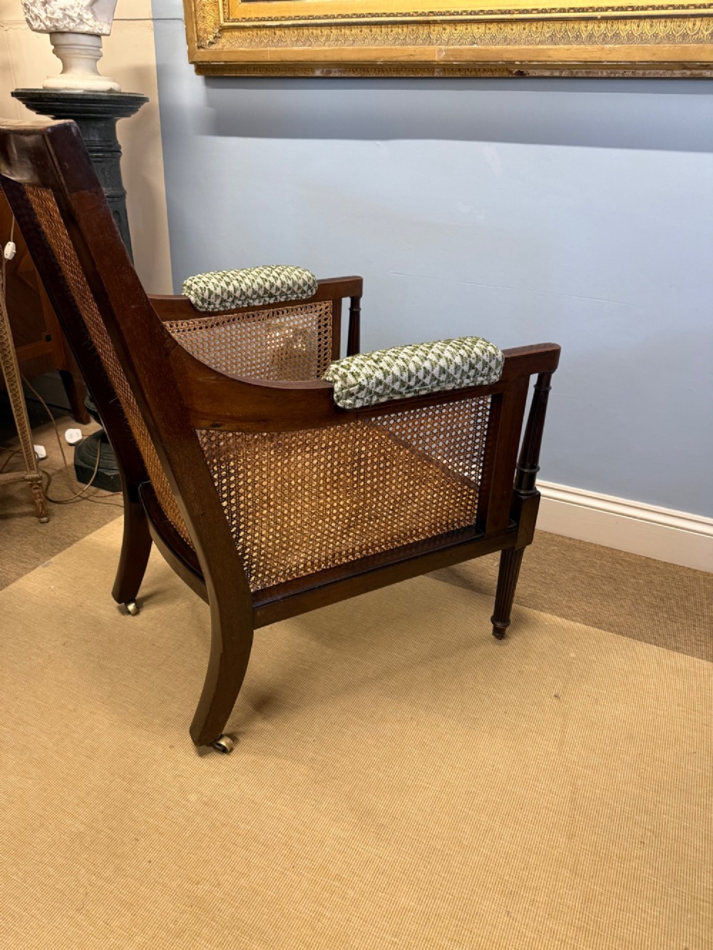 A late nineteenth-century dark mahogany Bergere armchair featuring woven cane side panels, fluted front legs on brass castors, and patterned upholstery. View II