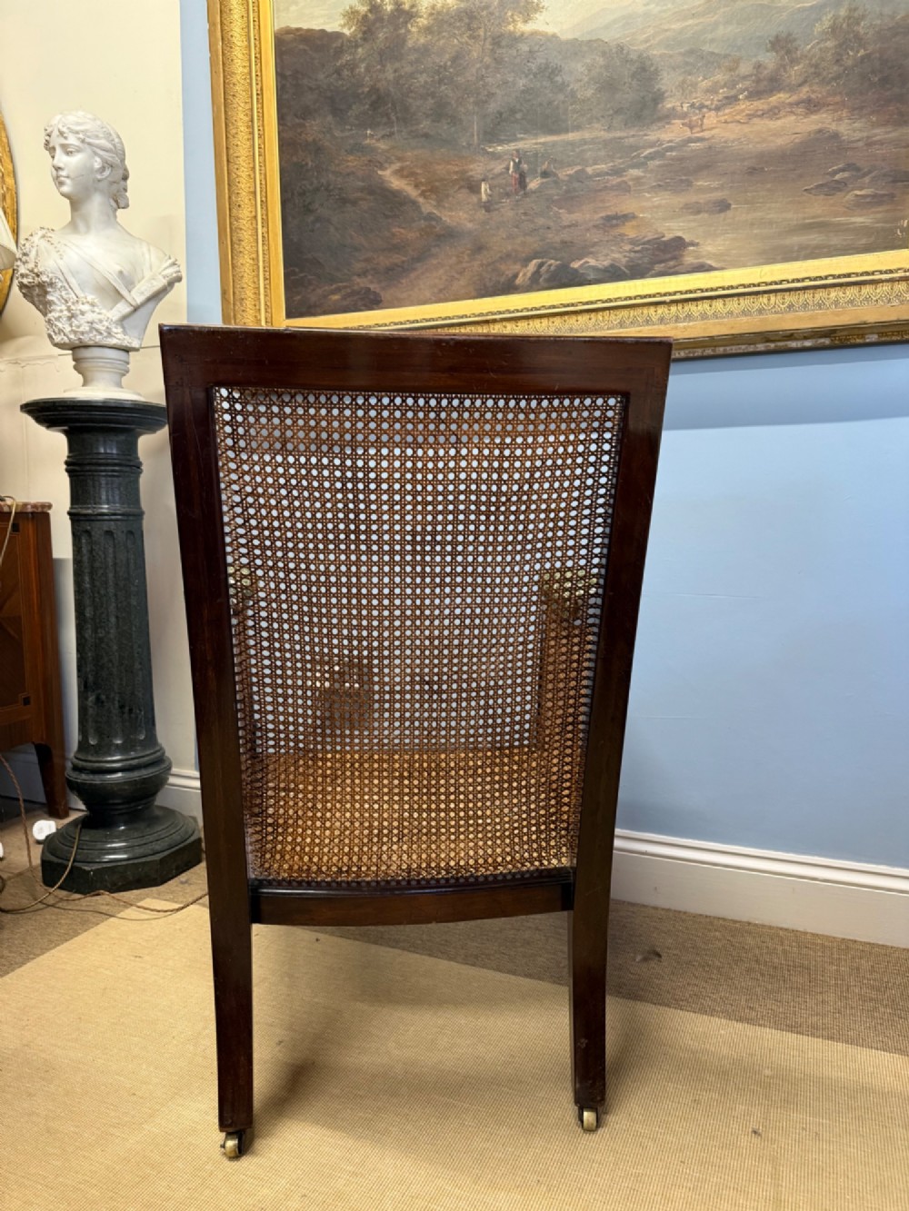 A late nineteenth-century dark mahogany Bergere armchair featuring woven cane side panels, fluted front legs on brass castors, and patterned upholstery. View III