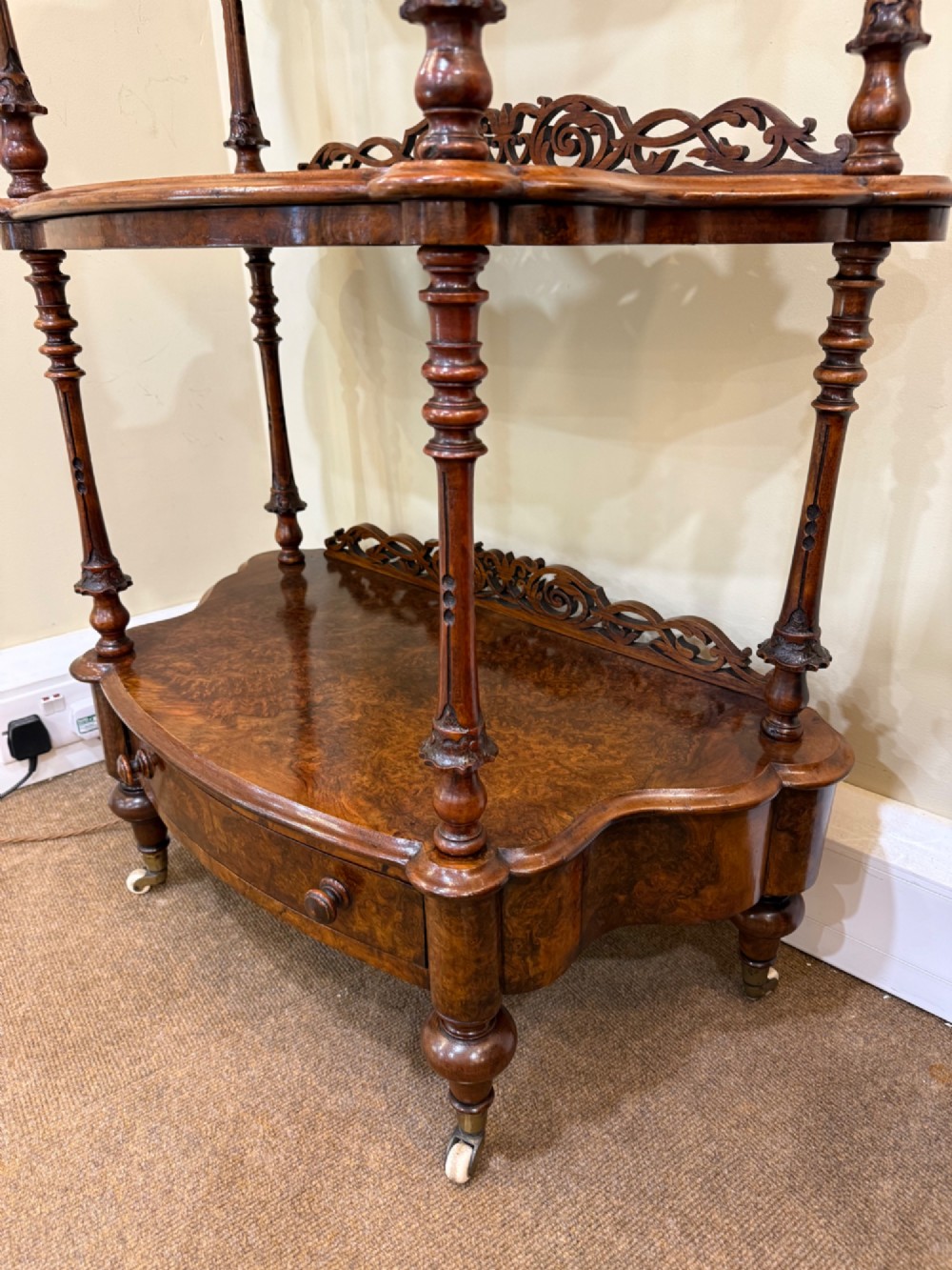 A three-tiered Victorian burr walnut whatnot featuring a carved fretwork upstand with a central arched mirror, turned spindle supports, and a base drawer on small castors. View III
