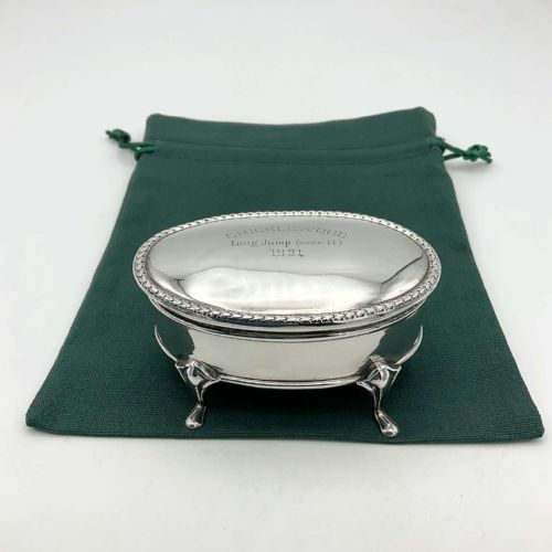fig 1. An oval sterling silver jewellery box featuring an engraved hinged lid, a foliage pattern border, and four curved cabriole feet.