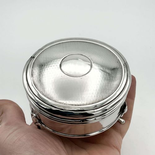 fig 2. A circular sterling silver jewellery box with engine-turned lid decoration and a central round cartouche, supported on three small feet.