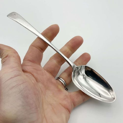 fig 1. An antique Georgian sterling silver dessert spoon featuring an oval bowl and a tapered stem with a crest engraved at the handle terminal.