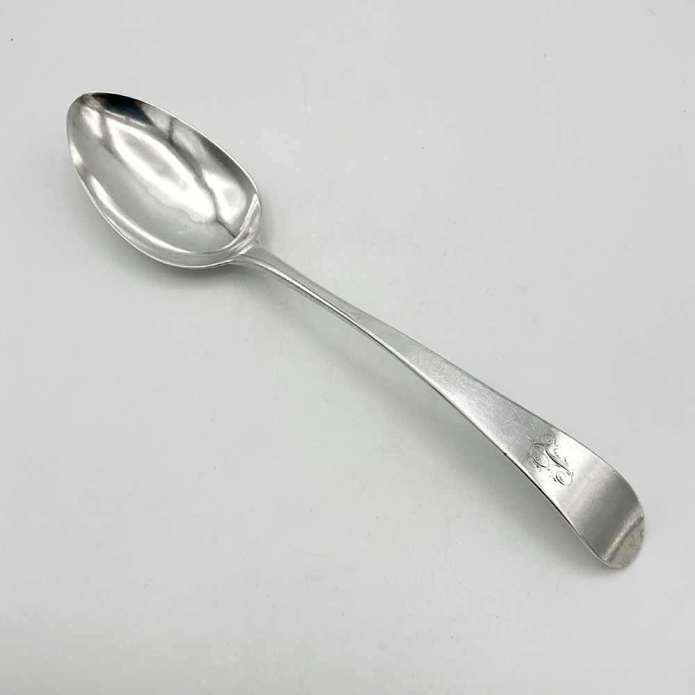 A Georgian sterling silver serving spoon with an oval bowl and a down-curved handle featuring an engraved monogram.