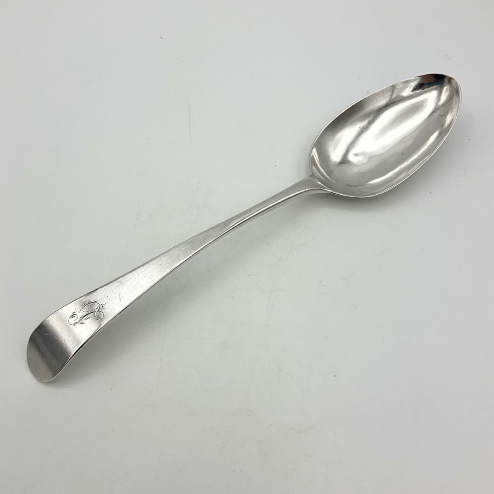 A Georgian sterling silver serving spoon with an oval bowl and a down-curved handle featuring an engraved monogram. View II