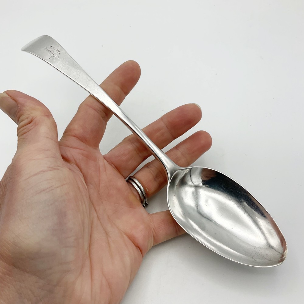 A Georgian sterling silver serving spoon with an oval bowl and a down-curved handle featuring an engraved monogram. View V