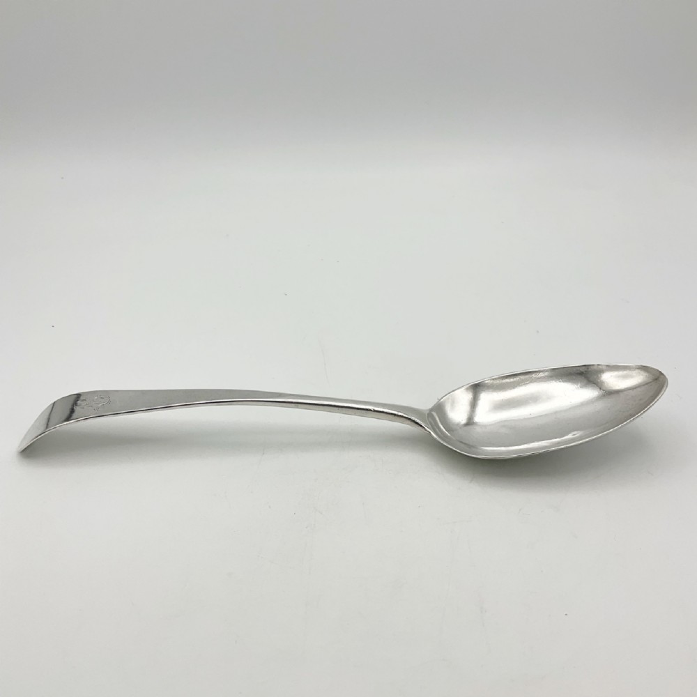 A Georgian sterling silver serving spoon with an oval bowl and a down-curved handle featuring an engraved monogram. View IX