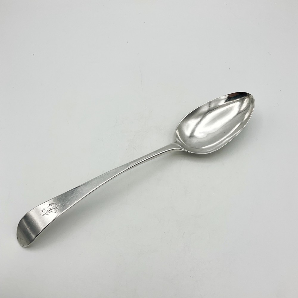 A Georgian sterling silver serving spoon with an oval bowl and a down-curved handle featuring an engraved monogram. View X