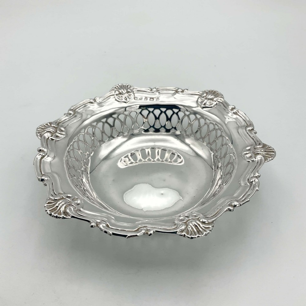A circular Edwardian sterling silver bon bon dish featuring intricate pierced lattice sides and a scalloped shell-motif rim.