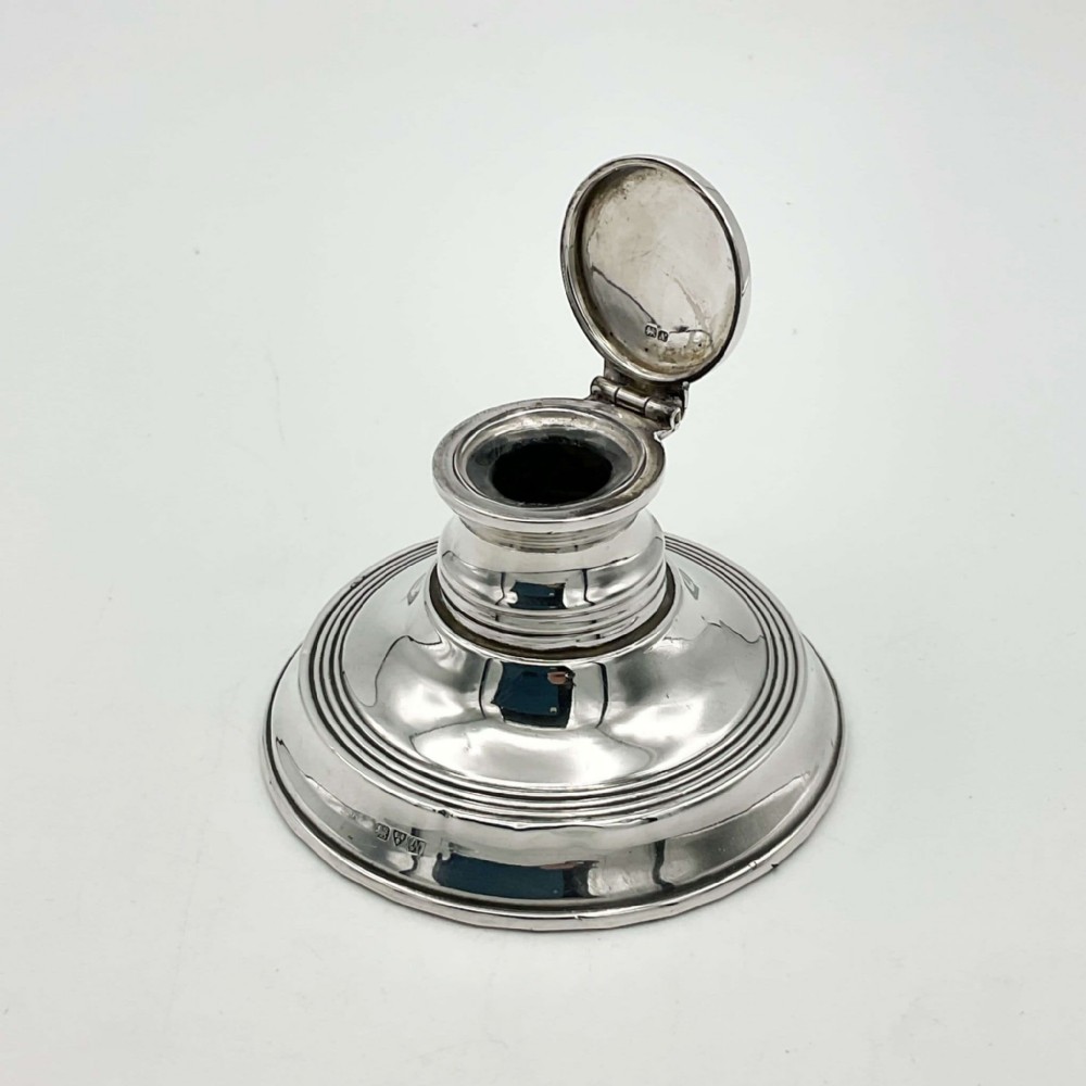 An antique circular sterling silver capstan inkwell with a open hinged lid and visible British hallmarks.