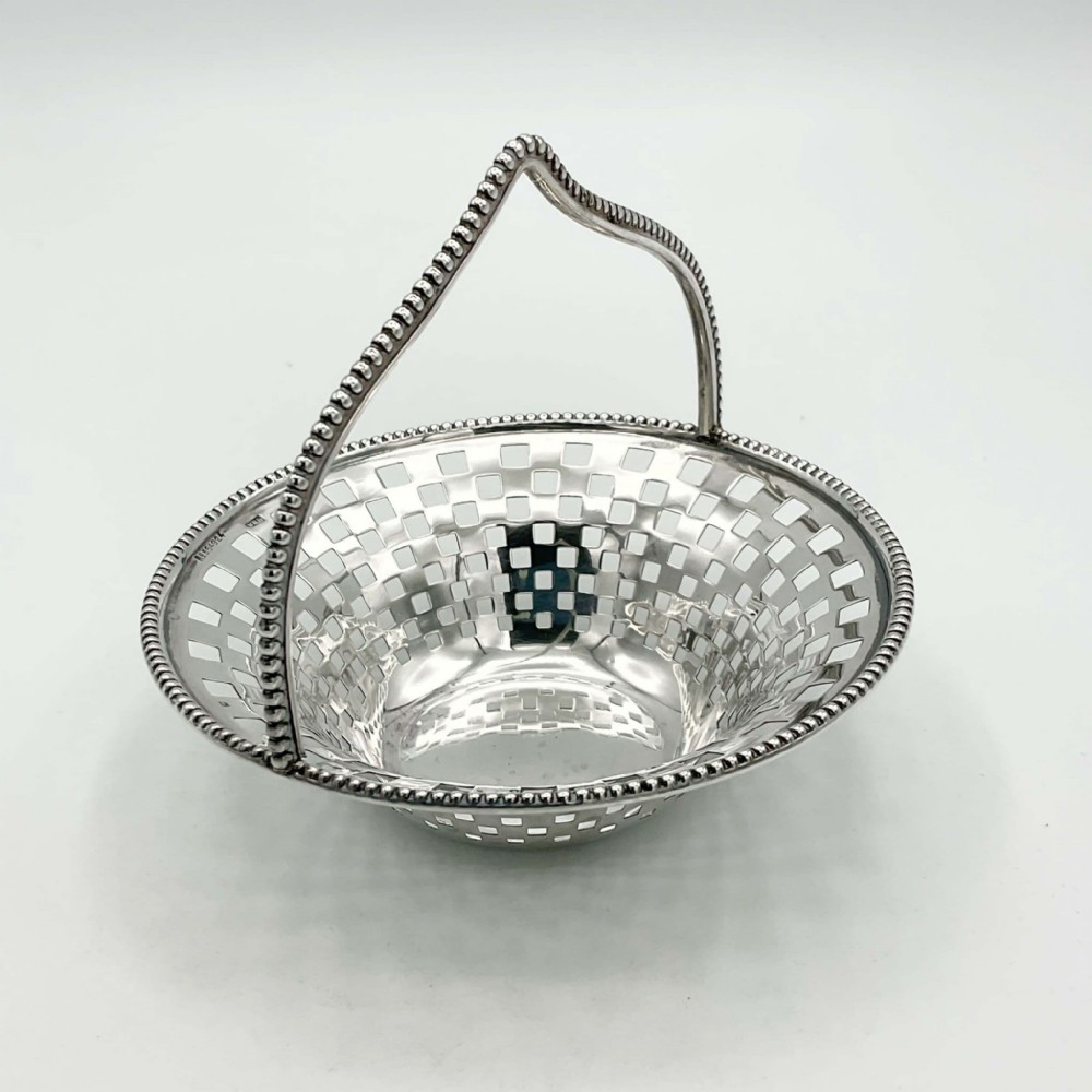 An Edwardian sterling silver basket with a pierced square lattice bowl, beaded rim, and an arched beaded handle.
