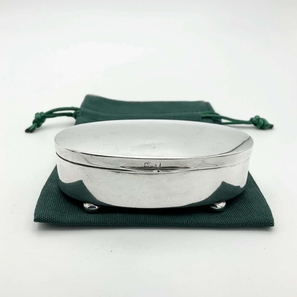 A polished oval sterling silver jewellery box with a hinged lid resting on four small rounded feet.