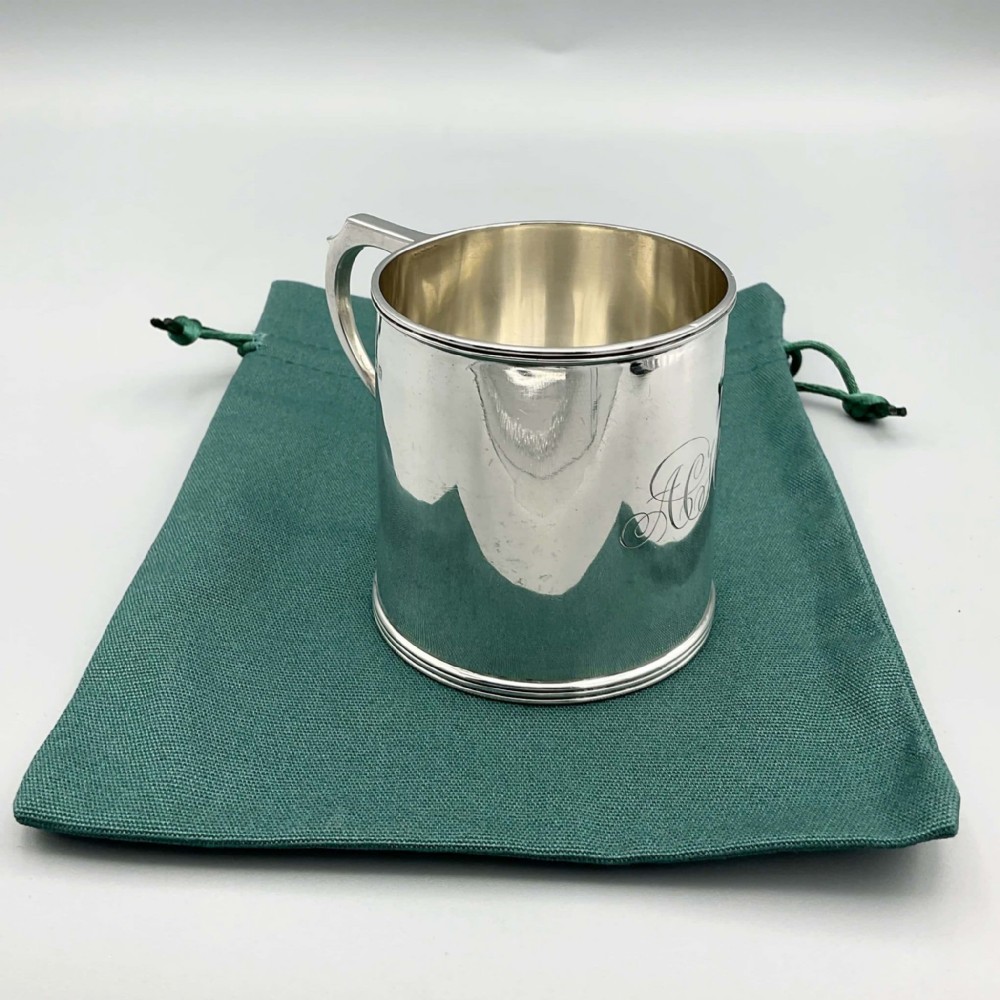 An Edwardian sterling silver christening cup with a cylindrical body, moulded rim, strap handle, and subtle monogram engraving.