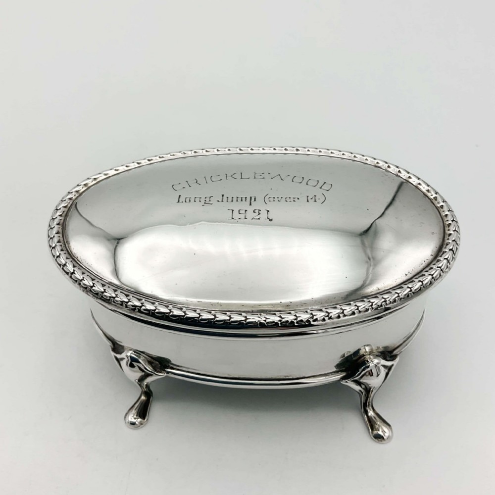 An oval sterling silver jewellery box featuring an engraved hinged lid, a foliage pattern border, and four curved cabriole feet.