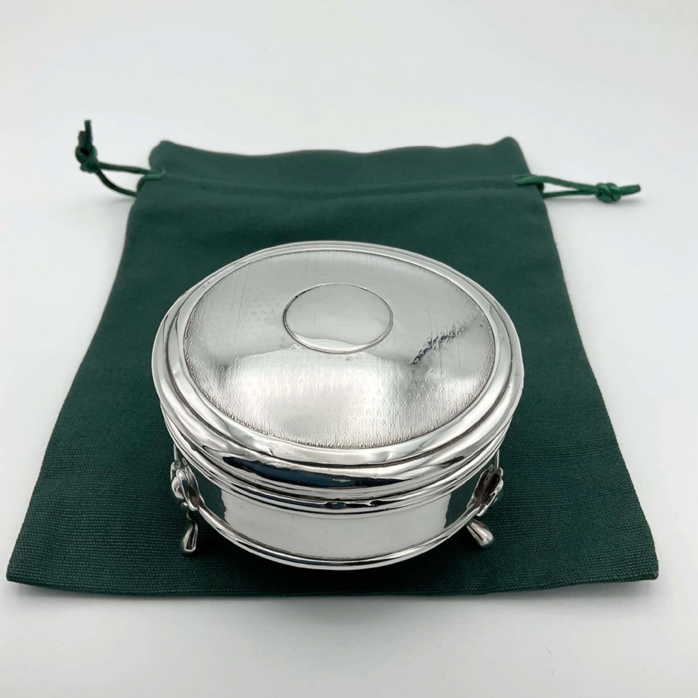 A circular sterling silver jewellery box with engine-turned lid decoration and a central round cartouche, supported on three small feet.
