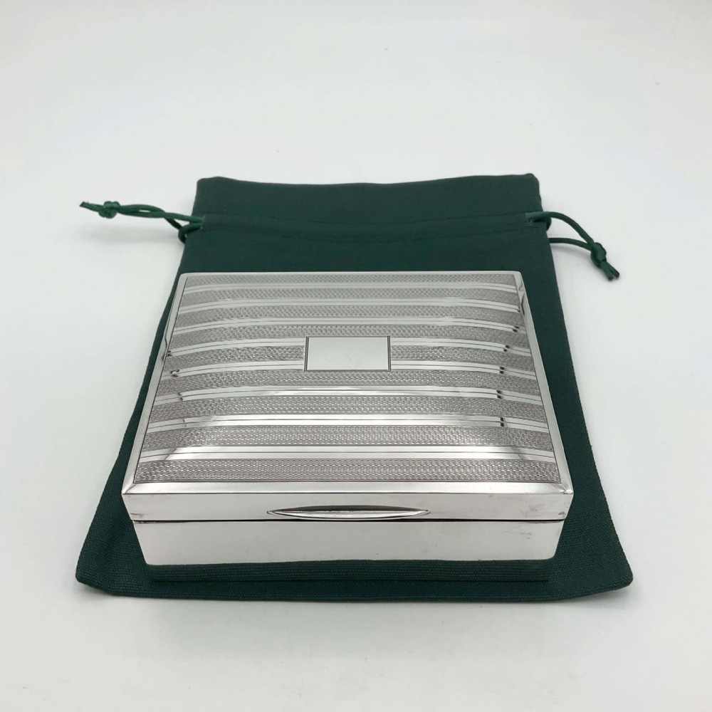 A rectangular Art Deco sterling silver box featuring an engine-turned striped pattern on the lid and a central rectangular vacant cartouche.