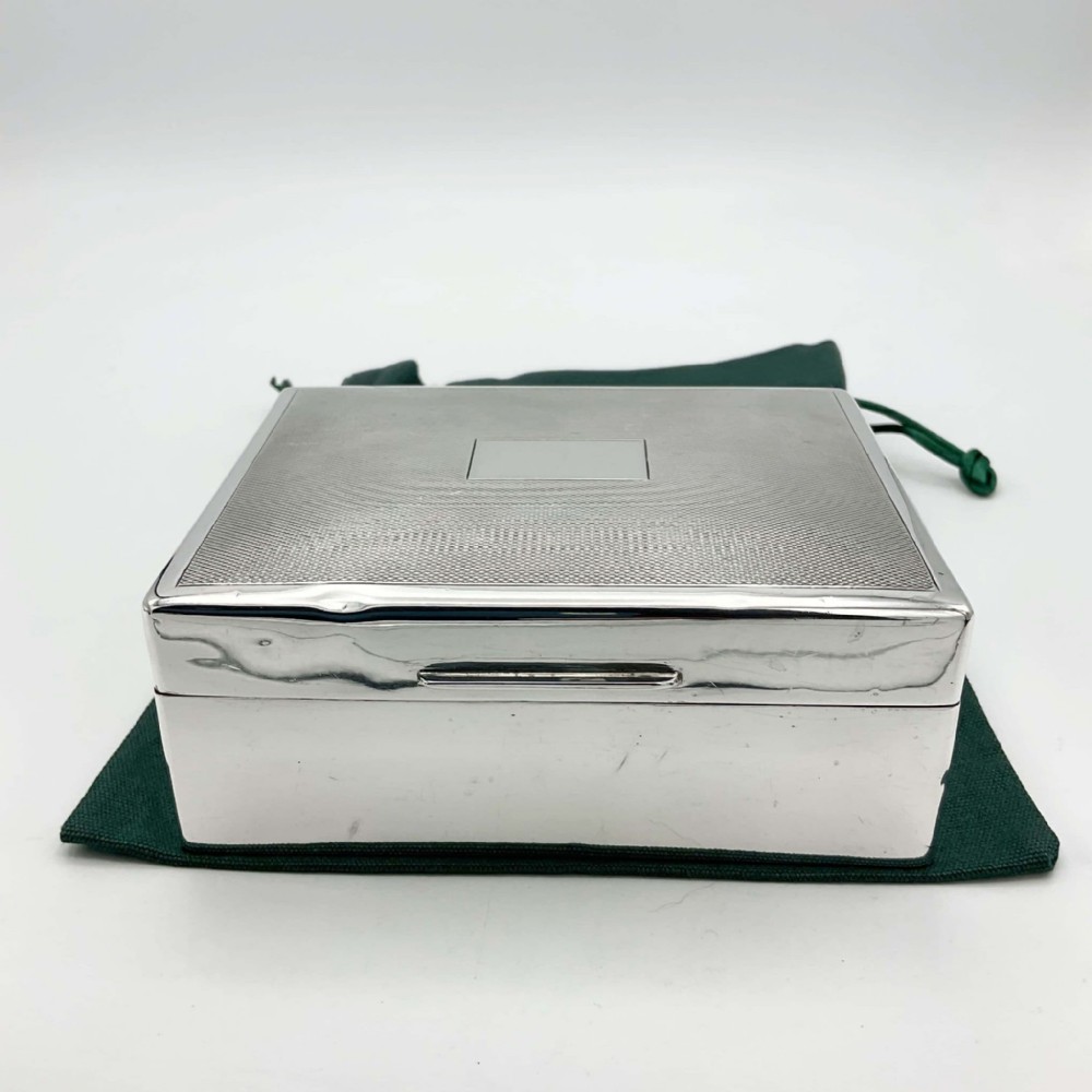 A square sterling silver box featuring an engine-turned pattern on the lid with a unengraved central rectangular cartouche.