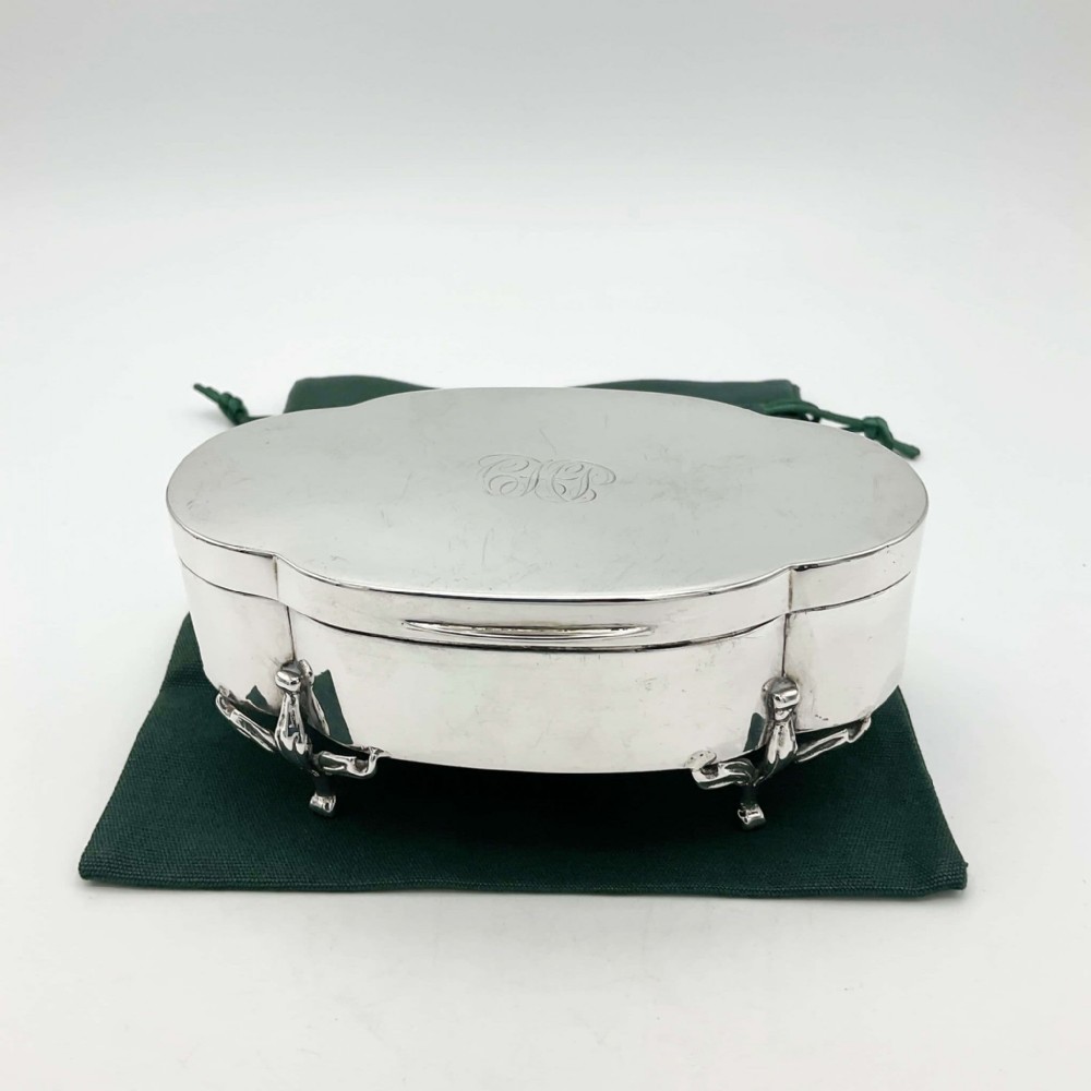 An oval 1918 sterling silver jewellery box featuring scrolled cabriole legs and an engraved monogram on the hinged lid.