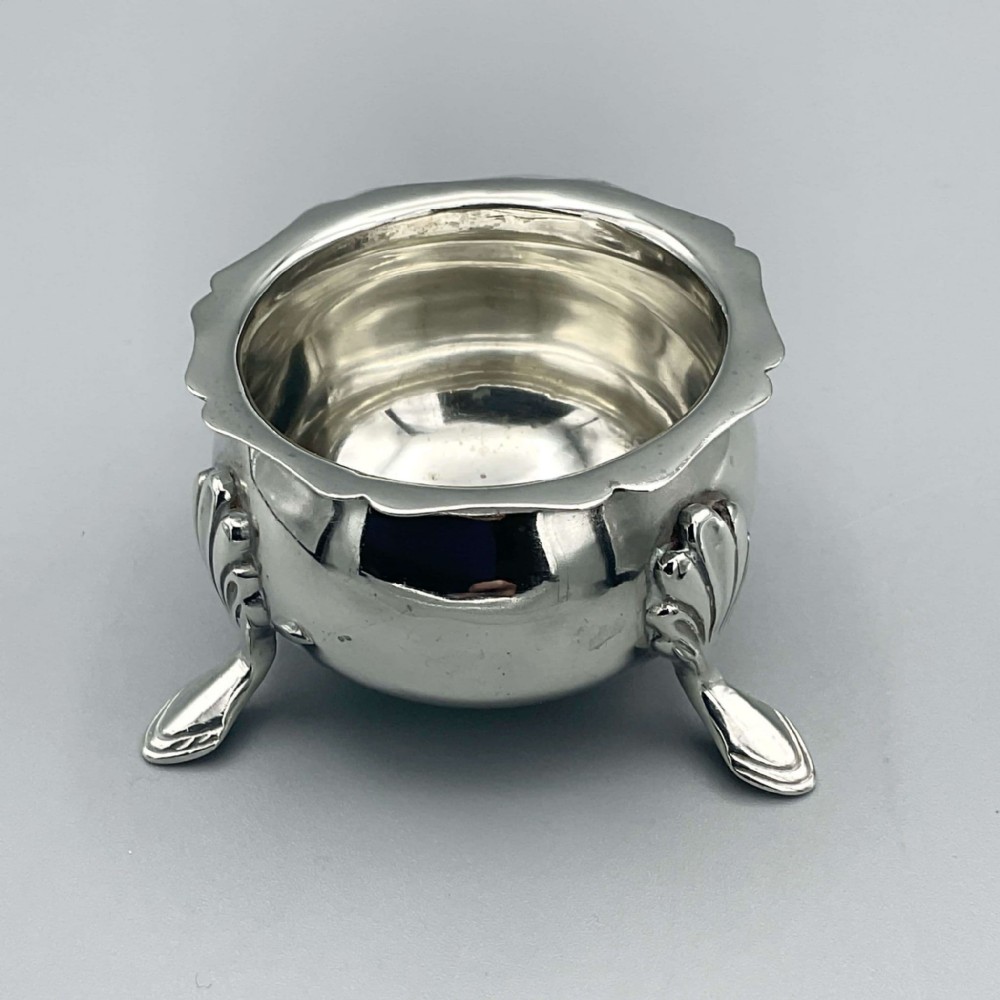 An Edwardian sterling silver salt bowl featuring a scalloped rim and three raised pad feet.