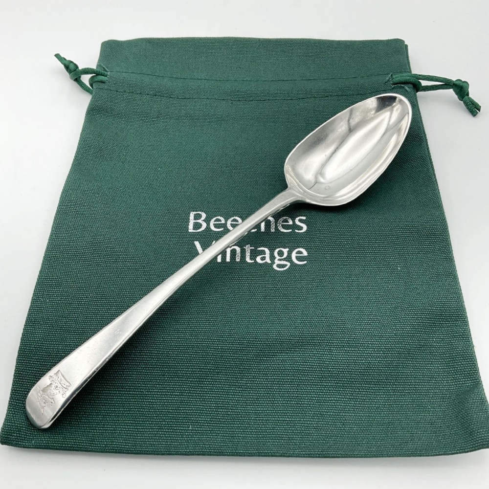 An antique Georgian sterling silver dessert spoon featuring an oval bowl and a tapered stem with a crest engraved at the handle terminal.