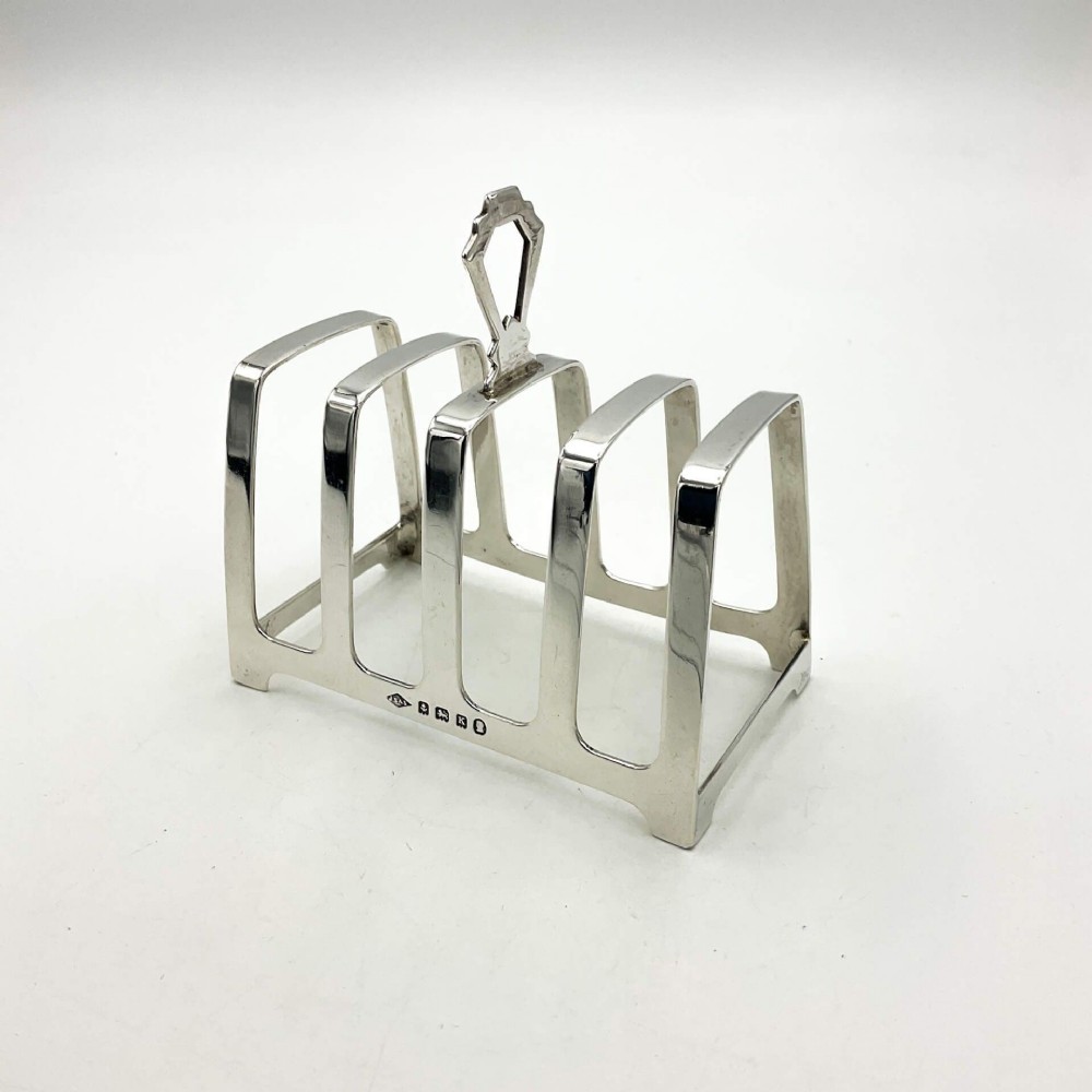 An Art Deco sterling silver toast rack featuring four slots with arched dividers, a central geometric handle, and visible hallmarks along the base.