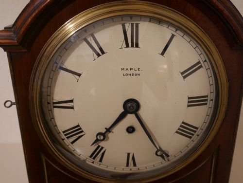 fig 1. An antique mahogany bracket clock featuring an arched hood, top brass handle, brass bracket feet, and a white dial with Roman numerals.