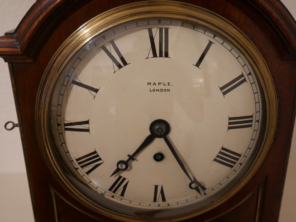 An antique mahogany bracket clock featuring an arched hood, top brass handle, brass bracket feet, and a white dial with Roman numerals. View II