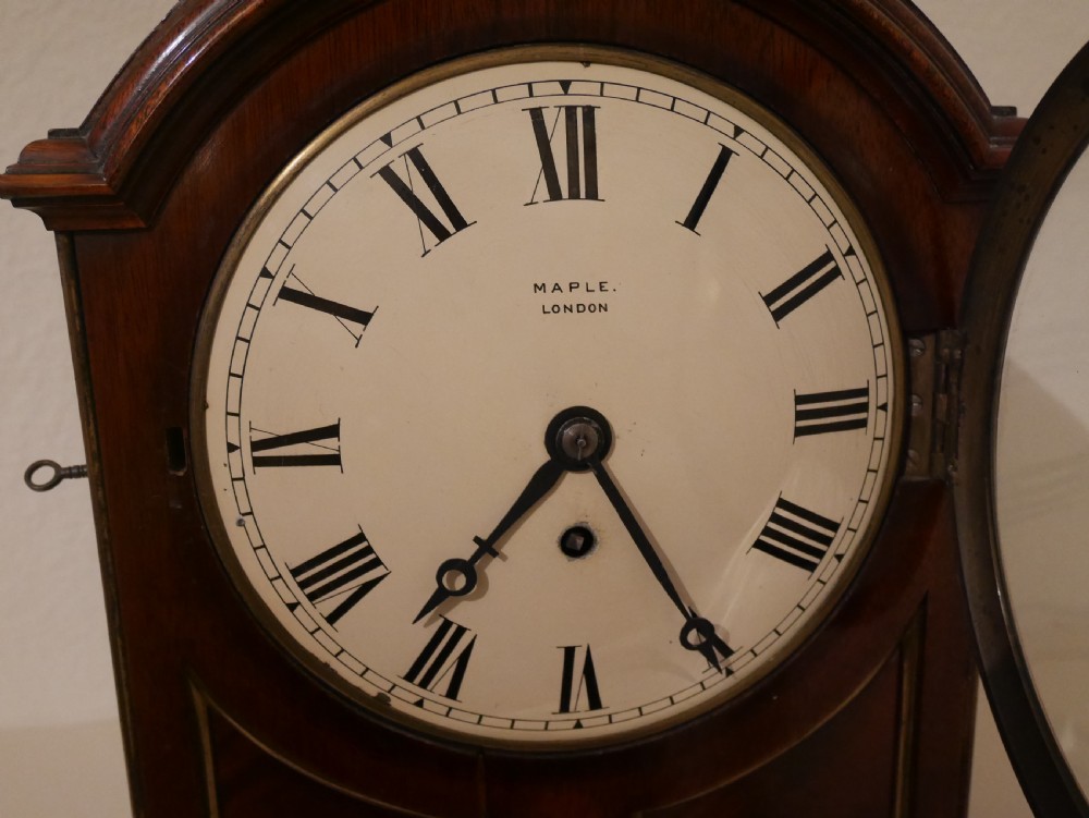 An antique mahogany bracket clock featuring an arched hood, top brass handle, brass bracket feet, and a white dial with Roman numerals. View III