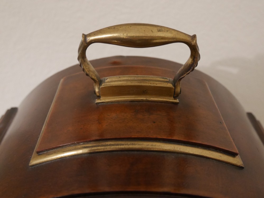 An antique mahogany bracket clock featuring an arched hood, top brass handle, brass bracket feet, and a white dial with Roman numerals. View IV