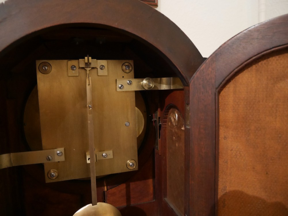 An antique mahogany bracket clock featuring an arched hood, top brass handle, brass bracket feet, and a white dial with Roman numerals. View VII