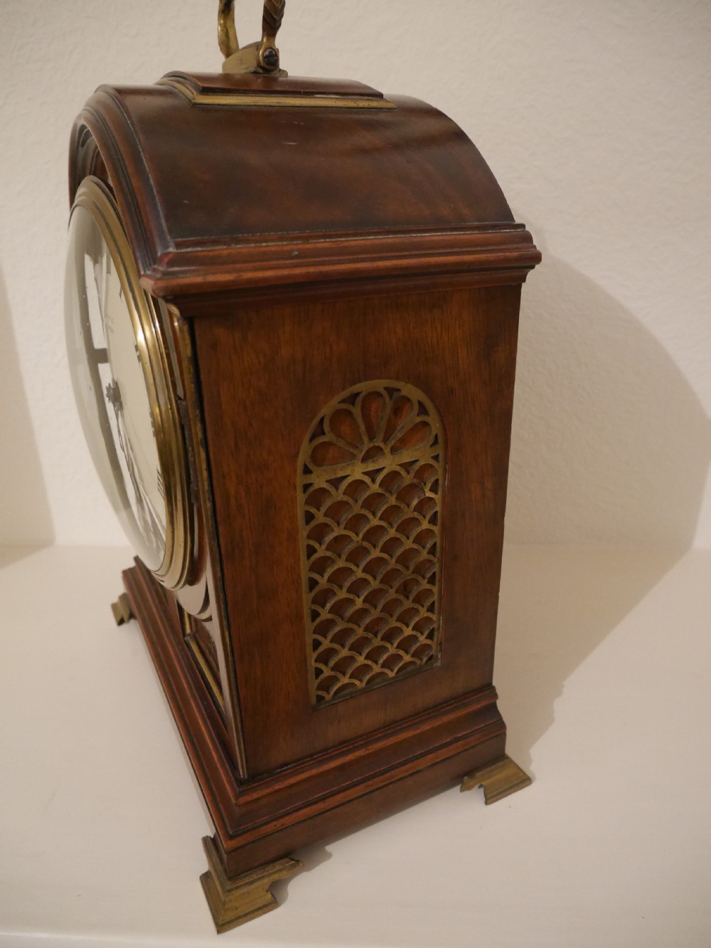 An antique mahogany bracket clock featuring an arched hood, top brass handle, brass bracket feet, and a white dial with Roman numerals. View VIII