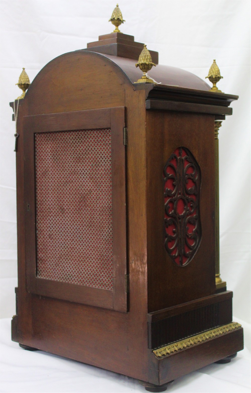 A dark mahogany Edwardian bracket clock featuring brass column supports, pineapple finials, and an ornate silvered dial with subsidiary chime indicators. View VI