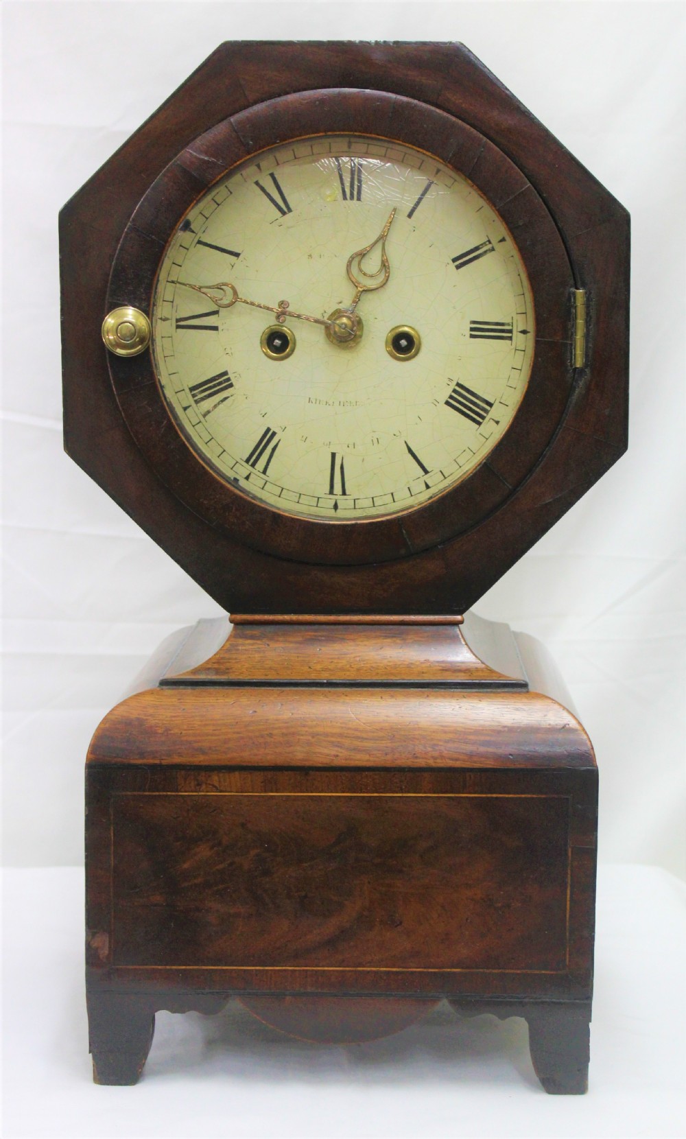An antique Scottish mahogany mantel clock featuring an octagonal upper head enclosing a cream painted dial with Roman numerals, set on a moulded base with bracket feet.