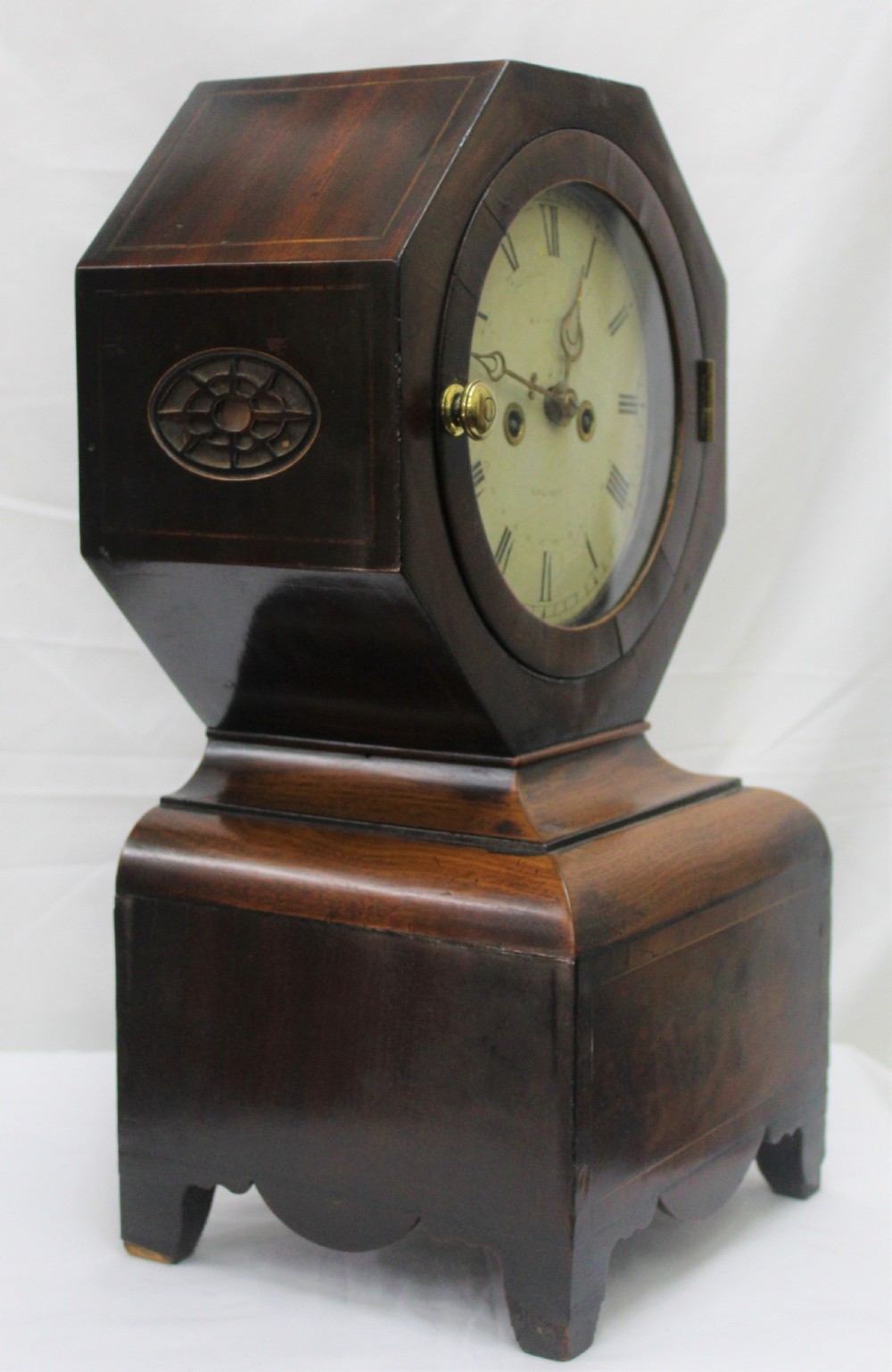 An antique Scottish mahogany mantel clock featuring an octagonal upper head enclosing a cream painted dial with Roman numerals, set on a moulded base with bracket feet. View II