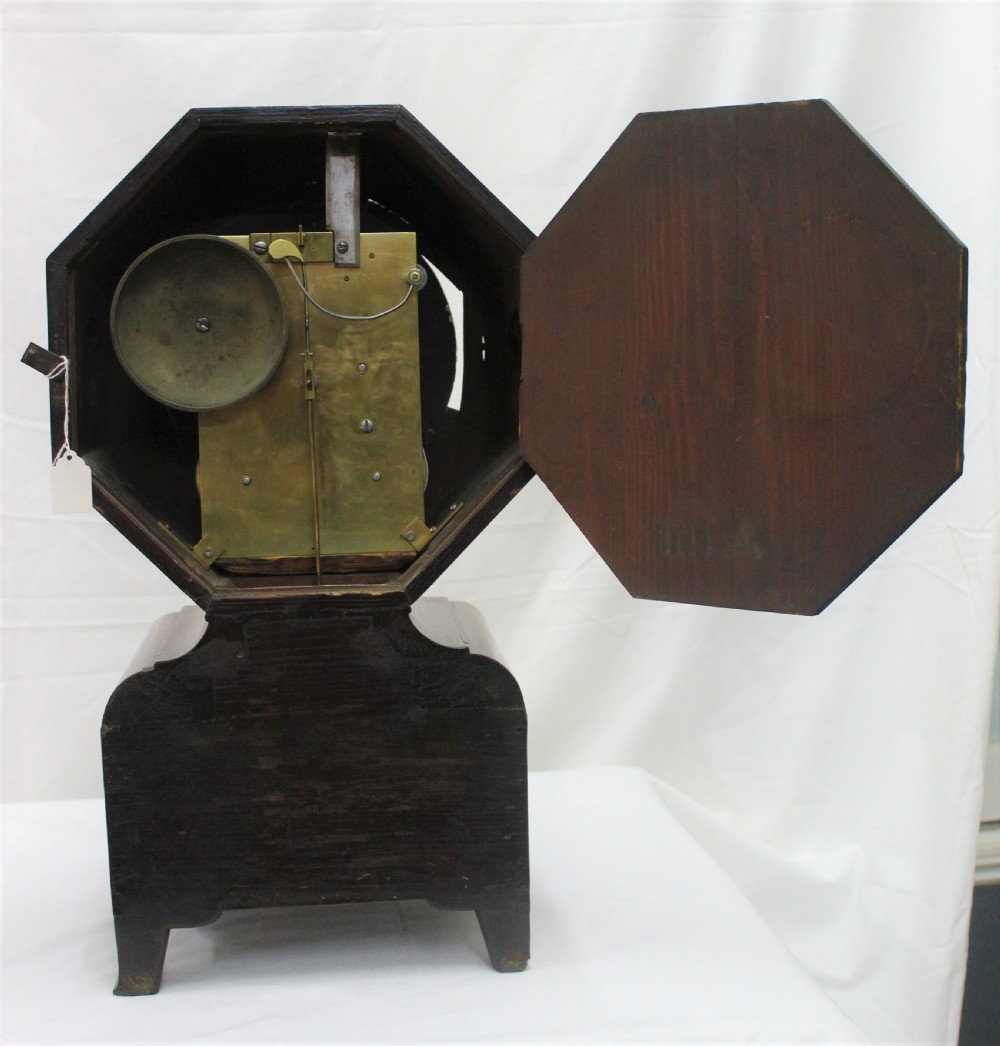 An antique Scottish mahogany mantel clock featuring an octagonal upper head enclosing a cream painted dial with Roman numerals, set on a moulded base with bracket feet. View V
