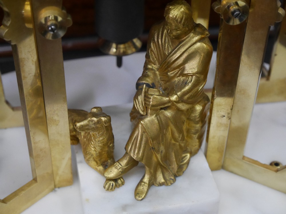 A Victorian brass skeleton clock designed in the shape of a Gothic spire, resting on a white marble base with a small seated figure at the bottom. View IX