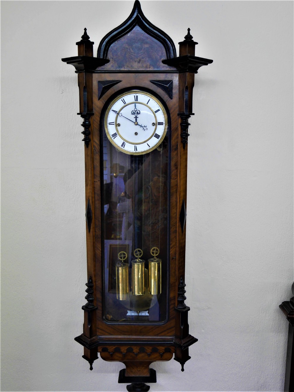 A 19th-century walnut Vienna regulator wall clock featuring a glazed front door, three brass weights, and a white enamel dial with Roman numerals.